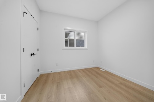 Bright white walls, wood-finish flooring, white window frame, and a white door with black hardware - 8915 Mayday Way Sw, Edmonton, AB - Indoor Photo Showing Other Room