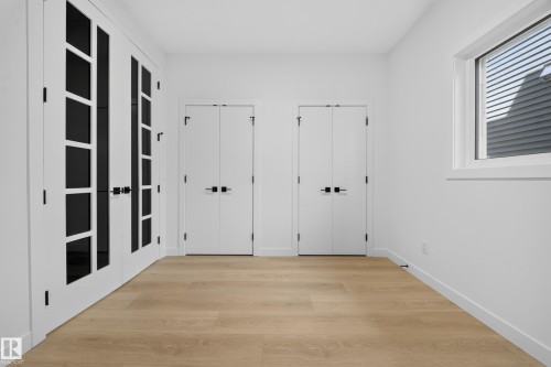 Light wood-finish flooring, white walls, clear-pane French doors with matte black hardware, and a single-pane window - 8915 Mayday Way Sw, Edmonton, AB - Indoor Photo Showing Other Room