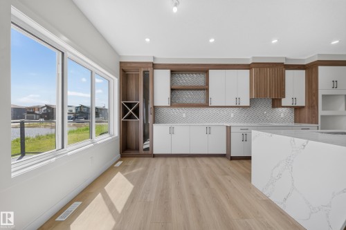 Modern kitchen featuring wood-finish flooring, white cabinetry, a built-in wine rack, and an island with a quartz countertop - 8915 Mayday Way Sw, Edmonton, AB - Indoor Photo Showing Kitchen
