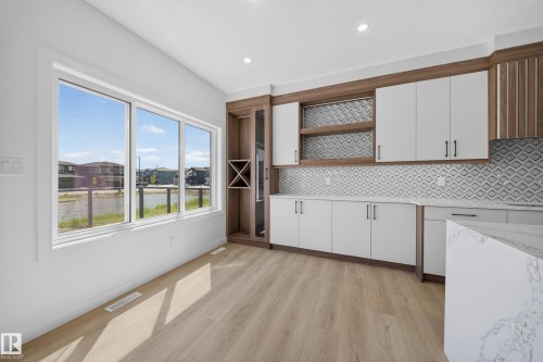 Expansive window, wood-finish flooring, white cabinetry, decorative backsplash, built-in shelving - 8915 Mayday Way Sw, Edmonton, AB - Indoor Photo Showing Kitchen With Upgraded Kitchen
