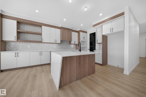 Kitchen featuring white cabinetry, wood-finish accents, white quartz countertops, a patterned tile backsplash, and wood-finish flooring - 8915 Mayday Way Sw, Edmonton, AB - Indoor Photo Showing Kitchen With Upgraded Kitchen