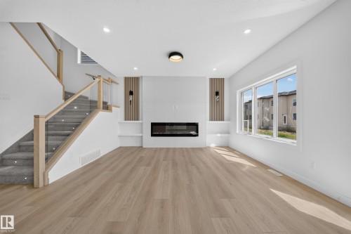 Wood-finish flooring, staircase with glass and wood railing, built-in electric fireplace, recessed lighting, and large multi-pane window - 8915 Mayday Way Sw, Edmonton, AB - Indoor With Fireplace