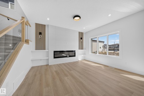 Spacious living area featuring wood-finish flooring, a linear electric fireplace with a tile surround, and built-in shelving - 8915 Mayday Way Sw, Edmonton, AB - Indoor Photo Showing Living Room With Fireplace