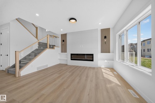 Contemporary living space featuring wood-finish flooring, a built-in electric fireplace, recessed lighting, and a modern staircase with glass paneling - 8915 Mayday Way Sw, Edmonton, AB - Indoor With Fireplace