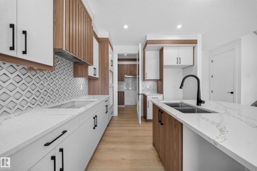 Open-concept kitchen featuring an island with double basin sink, light wood-finish and white cabinetry, patterned tile backsplash, and light-toned countertops - 8915 Mayday Way Sw, Edmonton, AB - Indoor Photo Showing Kitchen With Double Sink With Upgraded Kitchen