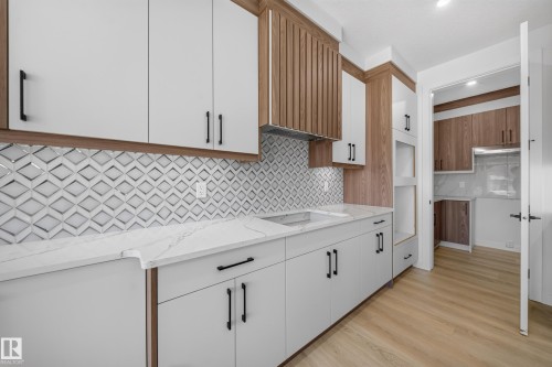 Modern kitchen featuring white cabinetry, wood-finish accents, a patterned tile backsplash, white countertops, and light wood-finish flooring - 8915 Mayday Way Sw, Edmonton, AB - Indoor Photo Showing Kitchen
