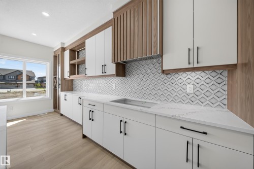 Modern kitchen featuring wood-finish open shelving, white cabinetry with matte black hardware, white quartz countertops, geometric tile backsplash, and light wood-finish flooring - 8915 Mayday Way Sw, Edmonton, AB - Indoor Photo Showing Kitchen