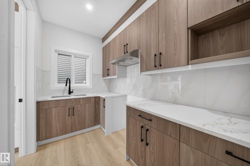 Wood-finish cabinetry with matte black hardware, white countertops, coordinating backsplash, and wood-finish flooring - 8915 Mayday Way Sw, Edmonton, AB - Indoor Photo Showing Kitchen With Double Sink