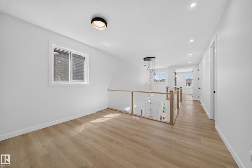 Light wood-finish flooring, glass panel railing with wood-finish top rail, recessed lighting, and a multi-pendant chandelier - 8915 Mayday Way Sw, Edmonton, AB - Indoor Photo Showing Other Room