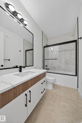 Modern vanity with wood-finish and white cabinetry, stone countertop, matte black fixtures, and a large mirror - 8915 Mayday Way Sw, Edmonton, AB - Indoor Photo Showing Bathroom