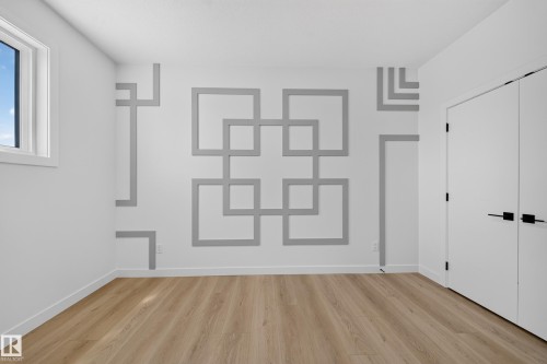 Architectural accent wall with geometric molding, wood-finish flooring, white walls, and a white window frame - 8915 Mayday Way Sw, Edmonton, AB - Indoor Photo Showing Other Room