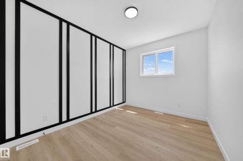 Wood-finish flooring, accent wall with vertical trim, white walls, flush mount lighting, and a double-pane window - 8915 Mayday Way Sw, Edmonton, AB - Indoor Photo Showing Other Room