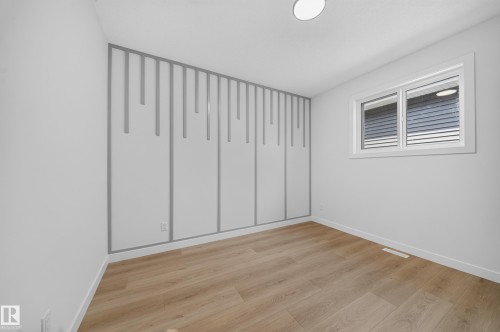 Room featuring a decorative accent wall, wood-finish flooring, and a single window with white trim - 8915 Mayday Way Sw, Edmonton, AB - Indoor Photo Showing Other Room