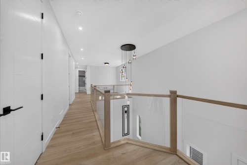 Wood-finish flooring, glass panel railing with wood trim, contemporary chandelier, recessed ceiling lighting, and white paneled doors with matte black hardware - 8915 Mayday Way Sw, Edmonton, AB - Indoor Photo Showing Other Room