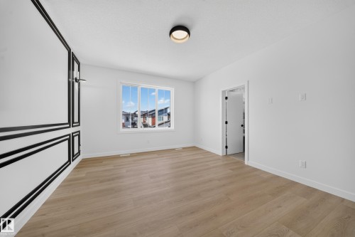 Wood-finish flooring, white walls with decorative black trim, large window, flush mount ceiling light, and interior doorway - 8915 Mayday Way Sw, Edmonton, AB - Indoor Photo Showing Other Room
