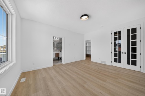 Spacious room featuring wood-finish flooring, a large window, a built-in closet with shelving, and French doors - 8915 Mayday Way Sw, Edmonton, AB - Indoor Photo Showing Other Room