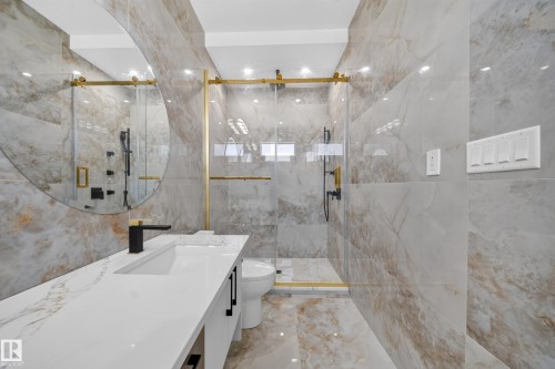 Full-height wall tiling, glass-enclosed shower with gold-tone accents, single vanity with integrated sink, gold-tone shower fixtures, and a large circular mirror - 8915 Mayday Way Sw, Edmonton, AB - Indoor Photo Showing Bathroom