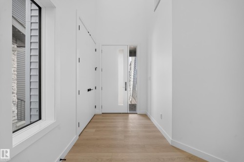 Light wood-finish flooring, white walls, built-in storage with matte black hardware, and a window with black trim - 8915 Mayday Way Sw, Edmonton, AB - Indoor Photo Showing Other Room