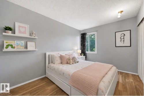 Serene secondary bedroom featuring soft gray walls, white built-in cabinetry with open shelving, wood-finish flooring, recessed ceiling lighting, and a large window with blackout drapery - #44 1415 62 St Nw, Edmonton, AB - Indoor Photo Showing Bedroom