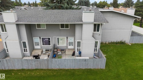 Rear townhouse exterior featuring a private fenced patio, grey horizontal siding, and a gabled roofline with a chimney - #44 1415 62 St Nw, Edmonton, AB - Outdoor With Exterior