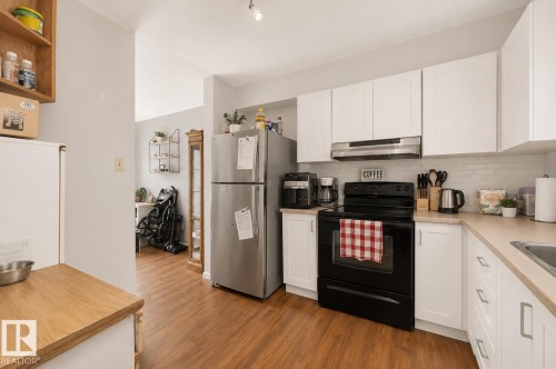 Kitchen featuring white shaker-style cabinetry, wood-finish flooring, a stainless steel refrigerator, and a black electric range with a coordinating range hood - #44 1415 62 St Nw, Edmonton, AB - Indoor Photo Showing Kitchen