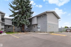 Exterior featuring horizontal siding, multiple windows, a paved parking area, and mature landscaping - 
