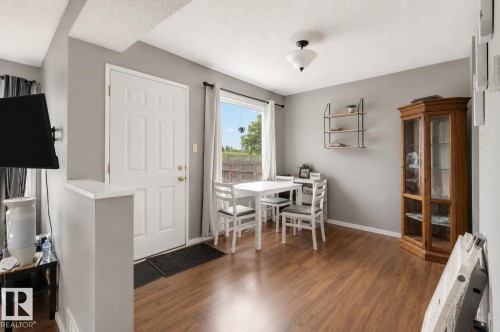 Wood-finish flooring throughout, featuring a multi-paneled white door, a wall-mounted light fixture, and a window with a curtain rod - #44 1415 62 St Nw, Edmonton, AB - Indoor Photo Showing Dining Room