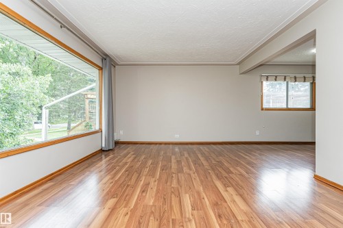 Spacious room featuring wood-finish flooring, light gray wall paint, and a prominent picture window with natural wood trim - 11139 62 Avenue Nw, Edmonton, AB - Indoor Photo Showing Other Room