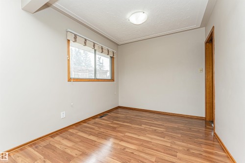 Wood-finish flooring with a light wood baseboard, neutral wall paint, and a window featuring wood trim - 11139 62 Avenue Nw, Edmonton, AB - Indoor Photo Showing Other Room