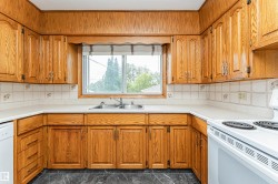 U-shaped kitchen with extensive wood cabinetry, light-toned countertops, a double basin stainless steel sink, tile backsplash, and dark-toned flooring - 