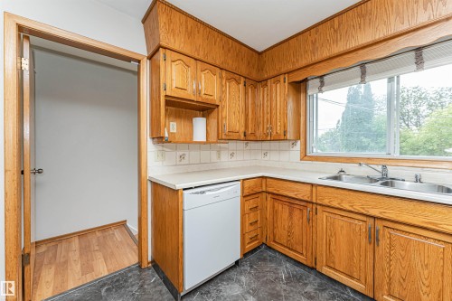 Wood cabinetry with brushed nickel hardware, white tiled backsplash, dual basin stainless steel sink, and a white dishwasher - 11139 62 Avenue Nw, Edmonton, AB - Indoor Photo Showing Kitchen With Double Sink