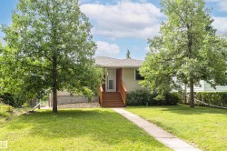 Manicured lawn, mature trees, concrete pathway, and wood-finish stairs leading to the entry - 