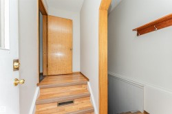 Wood-finish flooring with a wood-framed doorway, brass door hardware, and a wood wall shelf with metal hooks - 