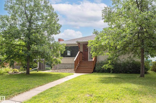 Front exterior featuring a concrete walkway, established lawn, mature trees, and a wood staircase leading to the entrance - 11139 62 Avenue Nw, Edmonton, AB - Outdoor