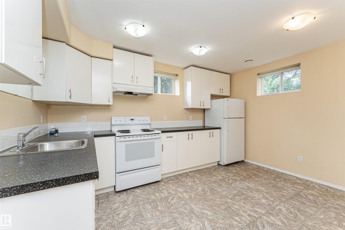 Kitchen featuring white cabinetry, dark speckled countertops, a white tile backsplash, and a stainless steel sink - 11139 62 Avenue Nw, Edmonton, AB - Indoor Photo Showing Kitchen