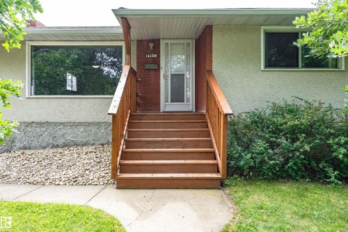 Wood-tone entry stairs with a simple railing, stucco exterior, and brick-clad accent wall - 11139 62 Avenue Nw, Edmonton, AB - Outdoor With Exterior