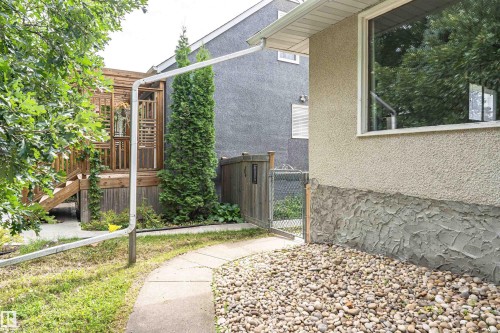 Exterior featuring stucco siding, a stone foundation, a paved pathway, a wooden deck structure, and established greenery - 11139 62 Avenue Nw, Edmonton, AB - Outdoor