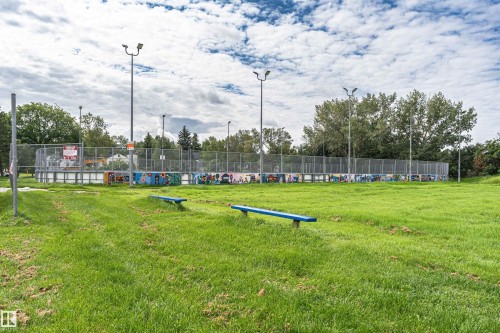 Manicured green space featuring two blue benches, surrounded by a chain-link fence with light posts - 11139 62 Avenue Nw, Edmonton, AB - Outdoor