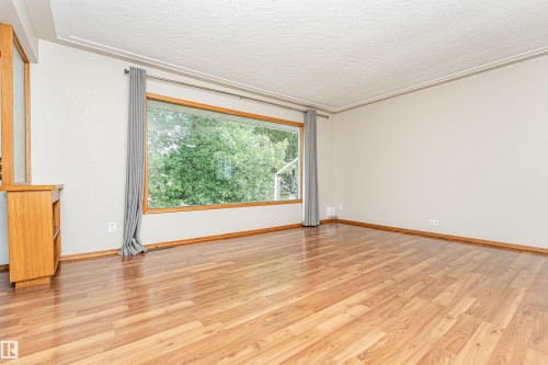 Wood-finish flooring throughout, large picture window with wooden trim, and built-in shelving unit - 11139 62 Avenue Nw, Edmonton, AB - Indoor Photo Showing Other Room