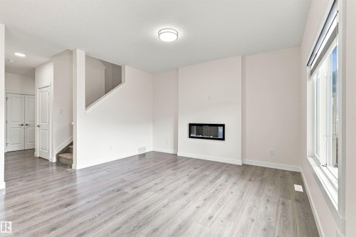 Recessed wall-mounted fireplace, wood-finish flooring, white walls, large window, and staircase with carpeted treads - 22019 82 Avenue Nw, Edmonton, AB - Indoor With Fireplace