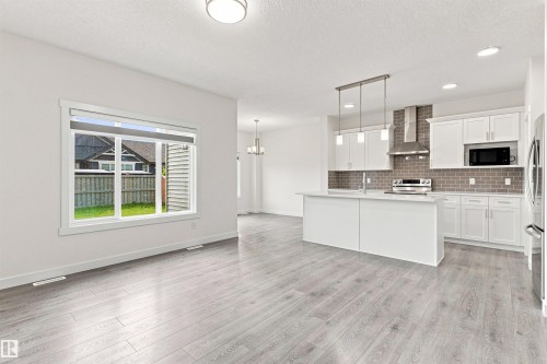 Open concept living space featuring wide plank wood-finish flooring, a kitchen island with pendant lighting, white cabinetry, stainless steel appliances, and a tiled backsplash - 22019 82 Avenue Nw, Edmonton, AB - Indoor Photo Showing Kitchen With Upgraded Kitchen
