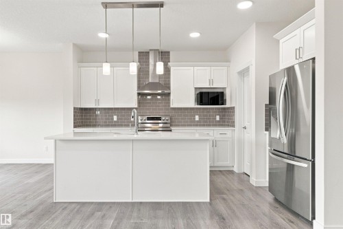 White cabinetry, stainless steel appliances, grey subway tile backsplash, white island with integrated sink, and wood-finish flooring - 22019 82 Avenue Nw, Edmonton, AB - Indoor Photo Showing Kitchen With Stainless Steel Kitchen With Upgraded Kitchen