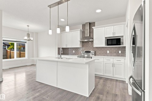 Kitchen featuring white cabinetry, a central island with a sink, stainless steel appliances, a subway tile backsplash, and wood-finish flooring - 22019 82 Avenue Nw, Edmonton, AB - Indoor Photo Showing Kitchen With Upgraded Kitchen