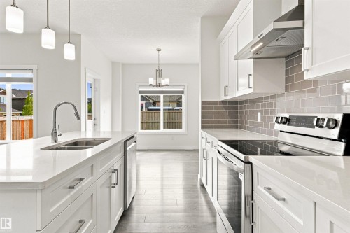 White shaker cabinetry with brushed nickel hardware, stainless steel appliances, light wood-finish flooring, white countertops, and a gray subway tile backsplash - 22019 82 Avenue Nw, Edmonton, AB - Indoor Photo Showing Kitchen With Stainless Steel Kitchen With Double Sink With Upgraded Kitchen