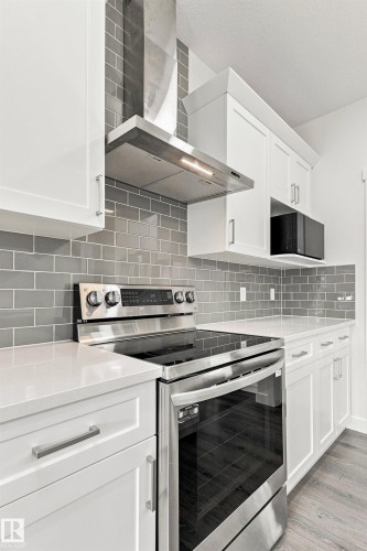 White shaker cabinetry, stainless steel range and hood, gray subway tile backsplash, white countertops, and wood-finish flooring - 22019 82 Avenue Nw, Edmonton, AB - Indoor Photo Showing Kitchen With Stainless Steel Kitchen With Upgraded Kitchen