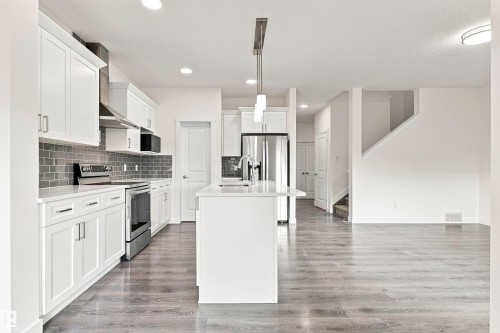 Modern kitchen featuring white cabinetry, stainless steel appliances, a white island, and wood-finish flooring - 22019 82 Avenue Nw, Edmonton, AB - Indoor Photo Showing Kitchen With Upgraded Kitchen