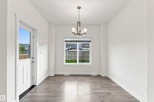 White paneled door with a glass insert, a window with white trim, wood-finish flooring, and a brushed nickel chandelier - 22019 82 Avenue Nw, Edmonton, AB - Indoor Photo Showing Other Room