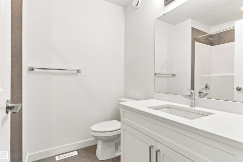 White vanity with an integrated rectangular sink and chrome faucet, large vanity mirror, white toilet, and a shower/tub combination with tiled surround - 22019 82 Avenue Nw, Edmonton, AB - Indoor Photo Showing Bathroom
