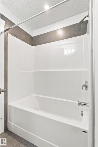 Bathtub with an integrated shower, tiled accent wall, and chrome fixtures - 22019 82 Avenue Nw, Edmonton, AB - Indoor Photo Showing Bathroom
