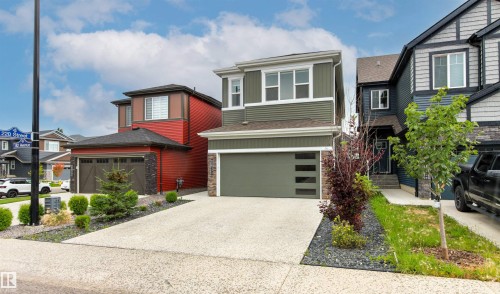 Two-story residential structure featuring a gray garage door with horizontal glass inserts, a concrete driveway, and landscaping with dark stone accents - 22019 82 Avenue Nw, Edmonton, AB - Outdoor With Facade